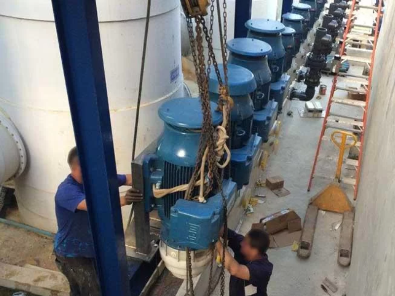 Dois homens brancos de uniforme azul instalando bomba centr&iacute;fuga em ind&uacute;stria